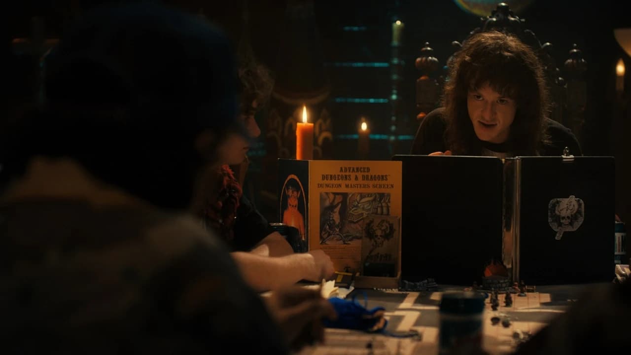 Cena da série Stranger Things: um mestre de cabelos longos atrás de um escudo de mestre de Advanced Dungeons & Dragons, com jogadores numa mesa à luz de velas e miniaturas.