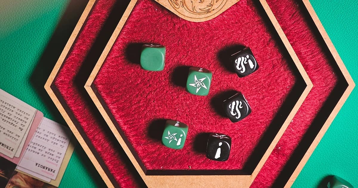 Bandeja hexagonal de feltro vermelho com dados verdes e pretos gravados com símbolos do Mythos, do jogo Cthulhu: Death May Die.