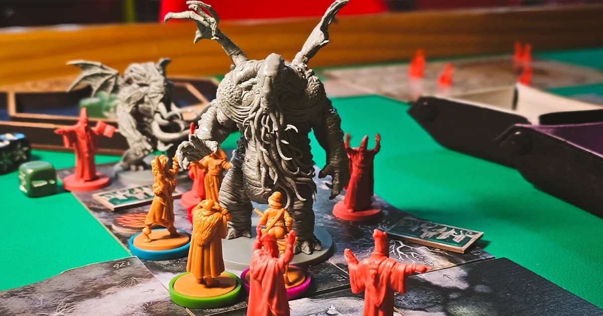 Tabuleiro de Cthulhu: Death May Die em jogo, com uma miniatura cinza de um Grande Antigo cercada por investigadores laranja e cultistas vermelhos.
