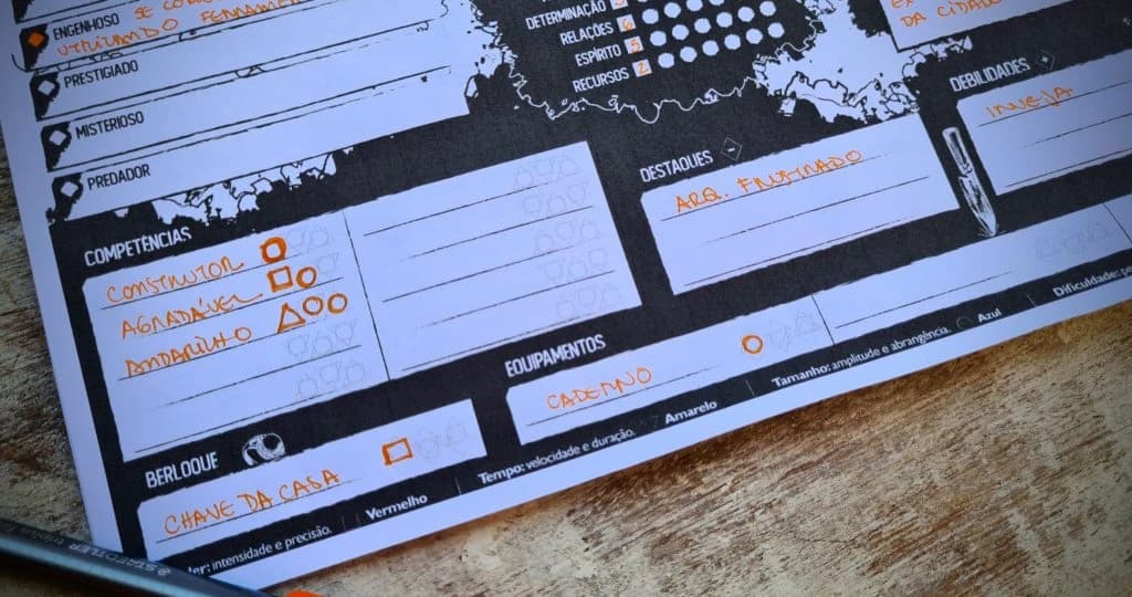Close de uma ficha de personagem preenchida à mão, com competências, equipamentos e berloque anotados em caneta laranja.