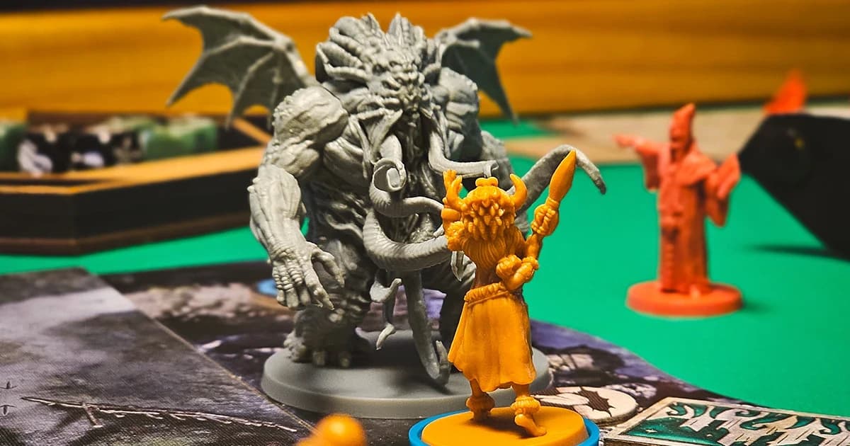 Close de uma miniatura cinza de Cthulhu encarando uma miniatura laranja de investigador com chifres, sobre o tabuleiro do jogo.